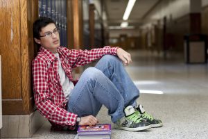 Young man sitting against a wall in school hallway